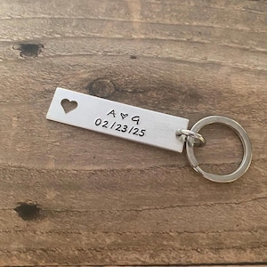 May include: Silver keychain with a heart cut-out and the inscription "A ♥ G 02/23/25".