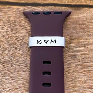 May include: A burgundy silicone watch band with a silver band engraved with the initials "K♥M".