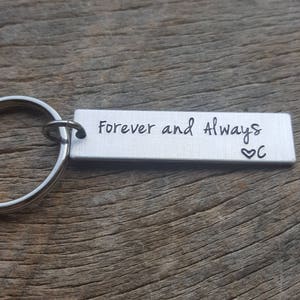 May include: Silver keychain with a rectangular tag that reads "Forever and Always" with a heart and the letter "C" engraved on it.