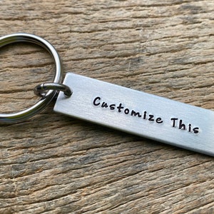 May include: Silver metal keychain with a rectangular tag that says "Customize This".