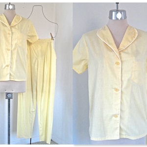 May include: A pale yellow pajama set, consisting of a short-sleeved button-down shirt with a white trim and a chest pocket, paired with matching pants. The set is displayed on a mannequin, showcasing the classic design.