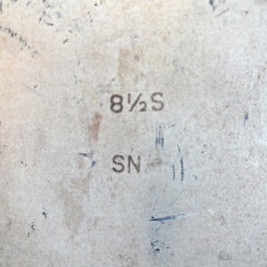 May include: Close-up of a shoe sole with the size marking "8 1/2 S" and the letters "SN" printed in black. The sole is a light beige colour with some wear and tear.