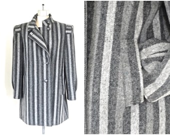 May include: A gray and white striped coat with a high collar and button closure. The coat has a tailored fit and long sleeves. The vertical stripes create a slimming effect. The coat is displayed on a mannequin.