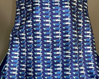 May include: A rectangular scarf featuring a repeating pattern of stylised birds in shades of blue, teal, and white against a dark blue background. The scarf has a solid dark blue border with a thin light blue trim along the top and bottom edges.