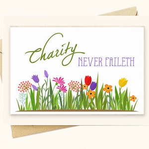 May include: A white card with green text that reads "Charity Never Faileth". The card is decorated with a border of colorful flowers.