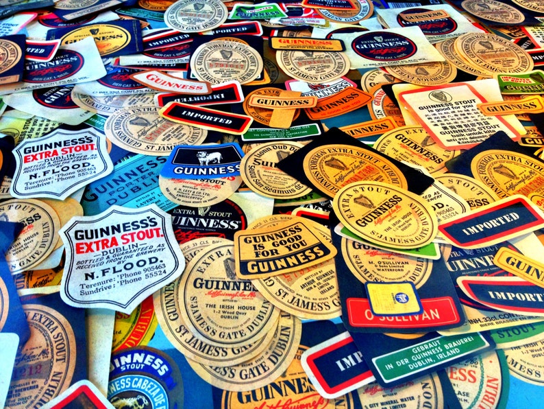 May include: A close-up of a collection of vintage Guinness beer bottle caps and labels. The caps are mostly brown and gold with black lettering. The labels are a mix of colors, including red, white, and blue. The labels feature the Guinness logo and text, including "Extra Stout", "Dublin", and "Imported".