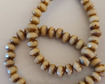 May include: A strand of cream-colored glass beads with brown stripes. The beads are faceted and have a slightly iridescent finish.