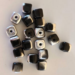 May include: A collection of square beads with a hole through the center. The beads alternate between a shiny silver and a glossy black finish. These beads are suitable for jewelry making and crafting projects.