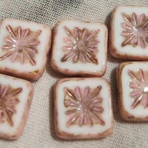 May include: Eight square-shaped glass beads with a pink and white floral design. The beads have a raised, textured pattern.