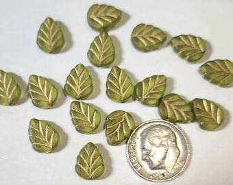 May include: A collection of small, leaf-shaped glass beads in a matte olive green finish with gold-toned detailing on the veins. A silver-colored United States dime is positioned next to the beads to provide a clear sense of scale for the items.