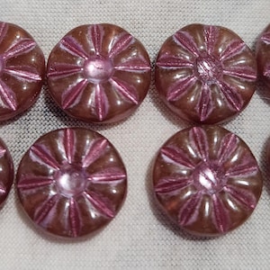 May include: Eight pink glass buttons with a flower design. The buttons have a raised center and a shiny finish.
