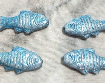 May include: Four small, individual fish-shaped ornaments or embellishments. Each piece features a metallic, pearlescent light blue finish with a textured, raised scale pattern across the body, a defined eye, and detailed fins on the top and bottom.