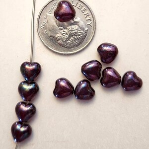 May include: A collection of heart-shaped beads in a deep purple color with iridescent highlights. Some beads are strung on a wire, while others are loose. A US dime is included for size reference. The beads have a glossy finish.