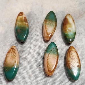 May include: Six oval-shaped beads with a glossy finish. The beads are a mix of colors, including teal, brown, and cream. Each bead has a hole for stringing. These beads are suitable for jewelry making.