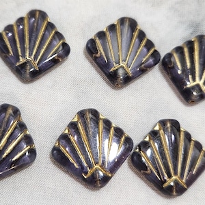 May include: Six decorative buttons with a seashell design. The buttons are a dark purple color with gold-colored accents. The buttons are square-shaped with a fan-like pattern.
