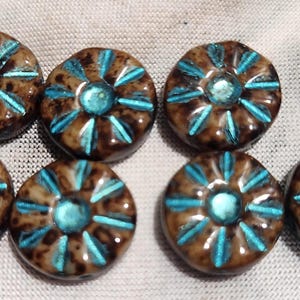 May include: Eight brown ceramic beads with a turquoise floral design. Each bead has a central turquoise circle surrounded by turquoise rays. The beads are round and have a glossy finish, perfect for jewelry making.