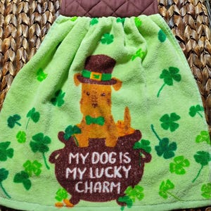 May include: Green kitchen towel with a brown pot, a dog wearing a green hat and a green bow tie, and the text "My dog is my lucky charm".