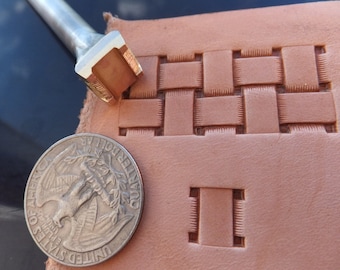 May include: A close-up of a leather stamping tool with a woven pattern. The tool is made of metal and has a wooden handle. The tool is being used to create a woven pattern on a piece of leather. The leather is a light brown color. A US quarter is included for scale.