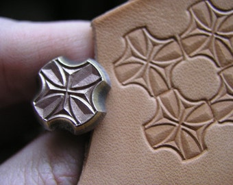 May include: A close-up of a metal leather stamping tool with a four-pointed star design. The tool is being used to create a pattern on a piece of leather.