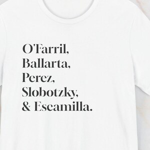 May include: White t-shirt featuring the names O'Farril, Ballarta, Perez, Slobotzky, and Escamilla in black text. The tee has a crew neck and is made from a soft fabric.