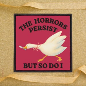 Puede incluir: Parche cuadrado con borde negro y fondo rojo. El parche presenta un ganso blanco sosteniendo una cuchara en su pico, con el texto "THE HORRORS PERSIST BUT SO DO I" en letras negras.