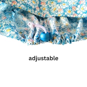 Puede incluir: Un gorro de ducha azul floral con flores blancas en forma de margarita. El gorro tiene un cord&oacute;n ajustable con una cuenta azul y la palabra "adjustable" impresa debajo.