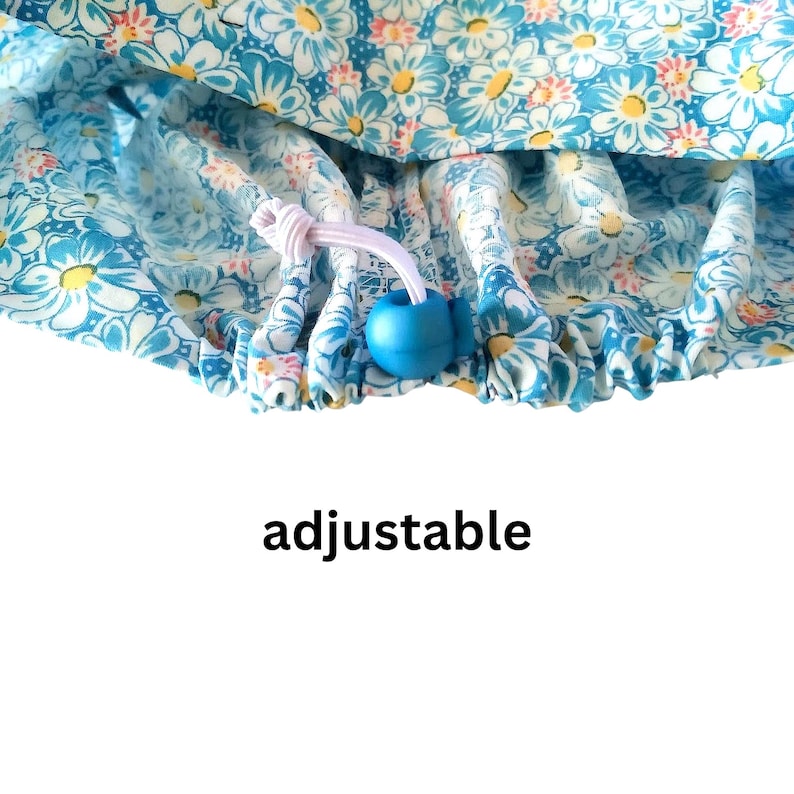 Puede incluir: Un gorro de ducha azul floral con flores blancas en forma de margarita. El gorro tiene un cord&oacute;n ajustable con una cuenta azul y la palabra "adjustable" impresa debajo.