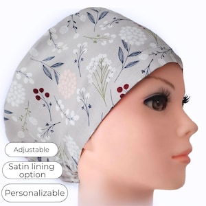 May include: A light gray surgical scrub cap with a floral pattern featuring white, pink, and burgundy flowers, and navy blue leaves. The cap has the text "Adjustable", "Satin lining option", and "Personalizable".
