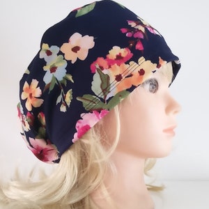 May include: A navy blue scrub hat with a floral print featuring pink, yellow, and white flowers. The hat has a ponytail opening in the back.