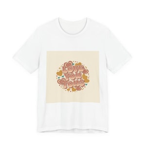 May include: White t-shirt with a retro design saying "Love You Tons". The design features hearts, stars, and dots in brown, gold, and teal, set on a cream background. The text is in a circular arrangement.
