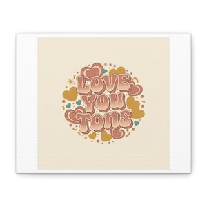 May include: A canvas print with the words "Love You Tons" in a retro font. The text is in pink and peach tones, encircled by hearts and stars in gold, teal, and pink. The background is a soft beige colour.
