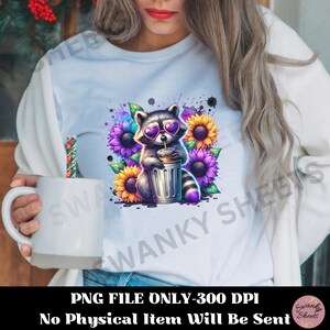 Pu&ograve; includere: Una maglietta bianca con una grafica colorata di un procione che indossa occhiali da sole e tiene una tazza. Il procione &egrave; circondato da girasoli e fiori viola. Il testo "PNG FILE ONLY-300 DPI" e "No Physical Item Will Be Sent" &egrave; stampato sotto la grafica.