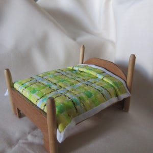 May include: A miniature wooden bed with a green, yellow, and blue patterned quilt. The bed frame is made of light brown wood with four tall, rounded posts. The quilt has a white border.