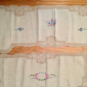 May include: Three white linen table runners with crocheted edges and embroidered floral designs in shades of pink, blue, and purple.
