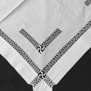 May include: White tablecloth with a delicate black lace border and intricate floral designs in the corners.