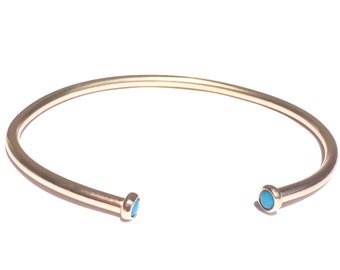 May include: A gold bangle bracelet with two turquoise stones on the ends.