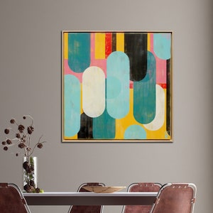 May include: Abstract art print with geometric shapes in shades of blue, yellow, pink, black, and white. The print is framed in a light wood frame and hangs on a gray wall above a dining table with brown leather chairs.