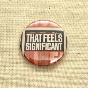 May include: A round button with the text "THAT FEELS SIGNIFICANT" in a bold, black font. The button has a red and white checkered pattern around the text and a glossy finish. The text "James & John Robins & Drew Masterman" is above the main text.