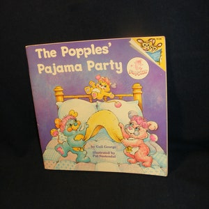 May include: A purple book cover with the title "The Popples' Pajama Party" and an illustration of three Popples in a bed. The book is by Gail George and illustrated by Pat Sustendal.