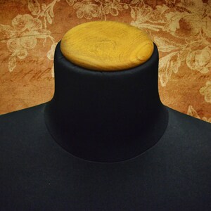 May include: A black fabric mannequin bust with a wooden top. The bust is used for displaying clothing and accessories.