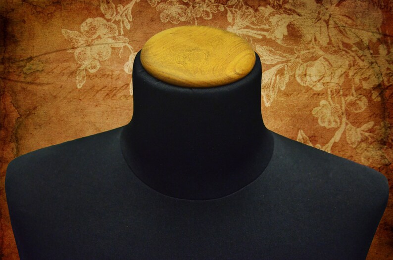 May include: A black fabric mannequin bust with a wooden top. The bust is used for displaying clothing and accessories.