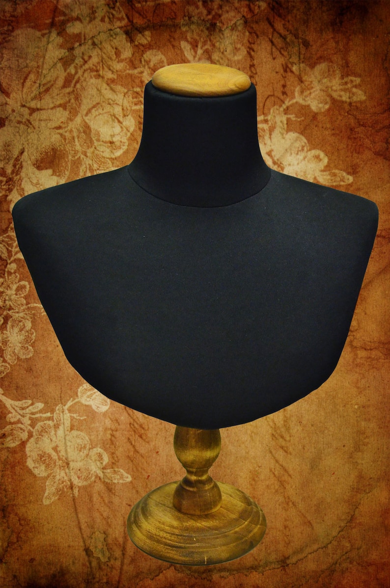 May include: A black fabric mannequin bust with a wooden base. The bust is on a brown background with a floral pattern.