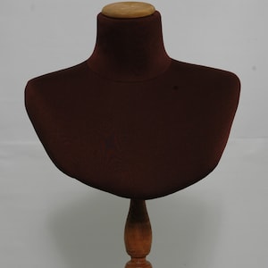 May include: A brown fabric bust form with a wooden base, designed for displaying necklaces or other jewelry.