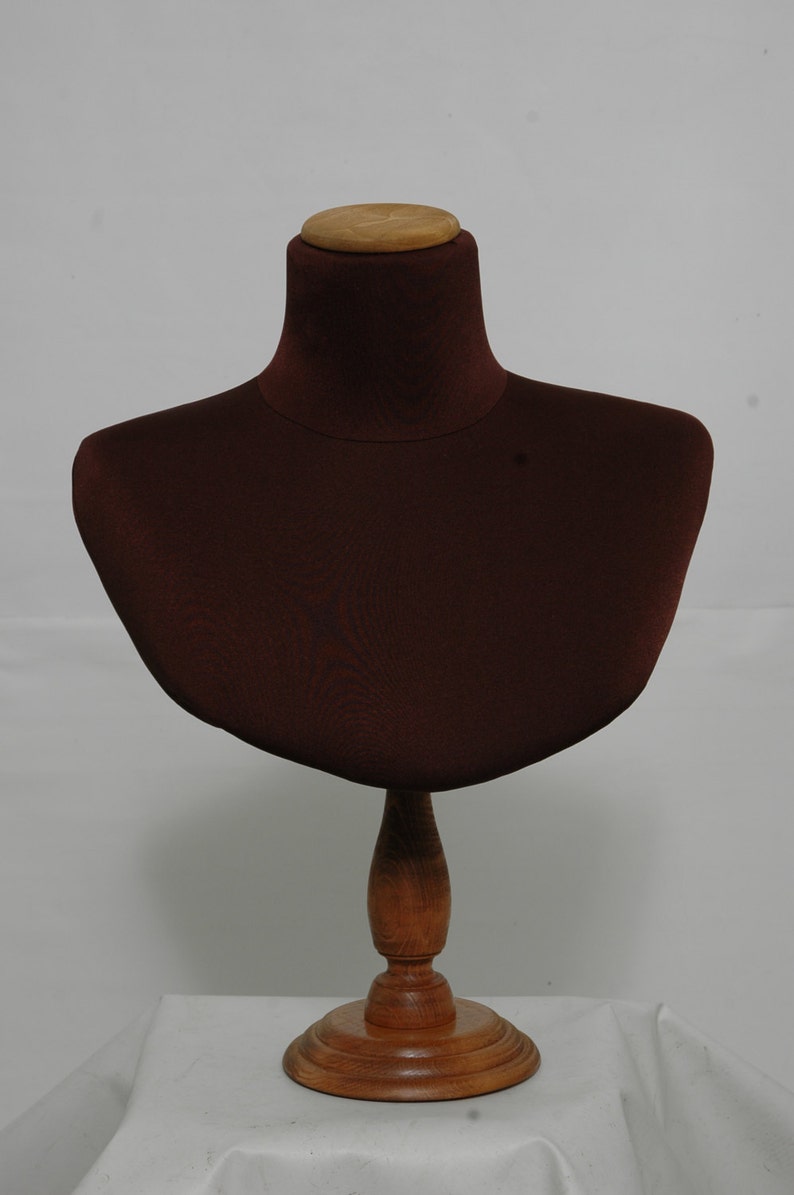 May include: A brown fabric bust form with a wooden base, designed for displaying necklaces or other jewelry.