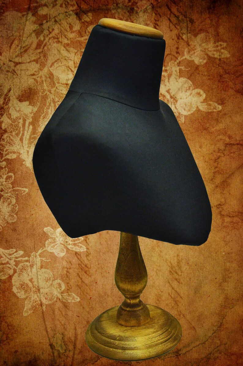 May include: A black fabric mannequin bust with a wooden base. The bust is on a brown background with a floral pattern.