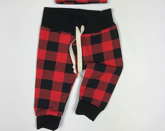Op de afbeelding: Rode en zwarte geruite babybroek met een bijpassende geruite, geknoopte muts.