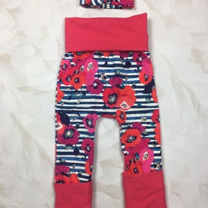 May include: A pair of red and white striped baby leggings with a floral print. The leggings have a wide elastic waistband and cuffed legs. A matching red headband with a white stripe is included.