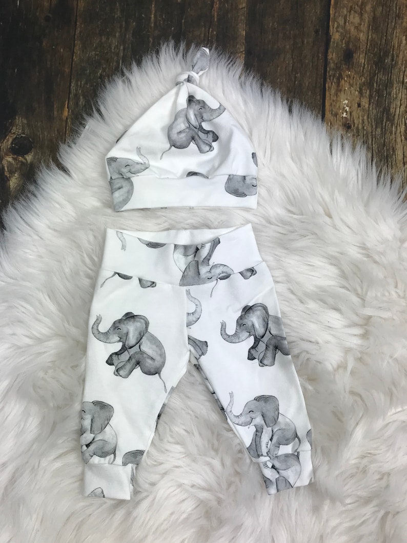 K&ouml;nnte beinhalten: Wei&szlig;e Baby-Leggings und eine M&uuml;tze mit einem grauen Elefanten-Druck.