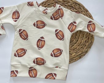 May include: A cream-colored long-sleeved shirt with a brown football pattern.