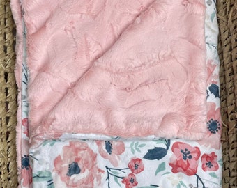 May include: A pink and white baby blanket with a floral pattern. One side of the blanket is soft and fuzzy, while the other side is made of a smooth fabric.